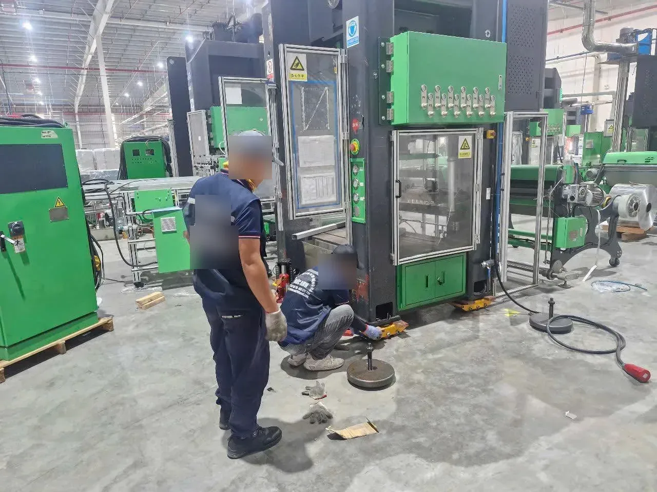 Thợ dùng kích thủy lực và con lăn di chuyển máy dập xanh đen trong xưởng sản xuất tại Xe Nâng Đức Anh