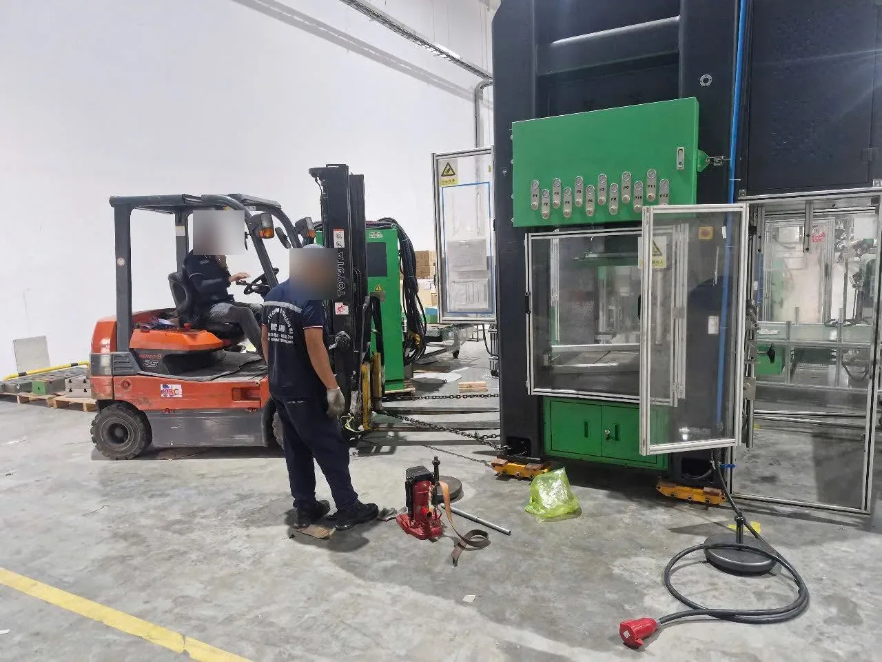 Xe nâng điện đứng cạnh máy dập đang trượt trên con lăn qua sàn xưởng tại Xe Nâng Đức Anh