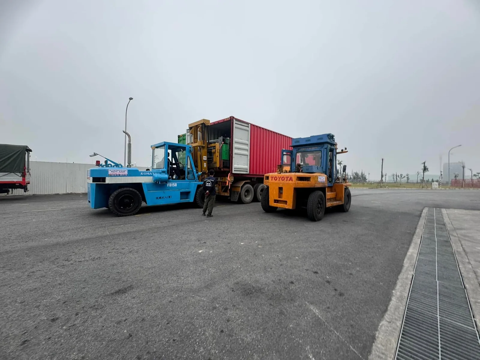Xe nâng Komatsu và Toyota đứng hai bên đuôi container có người chỉ huy điều phối tại Xe Nâng Đức Anh