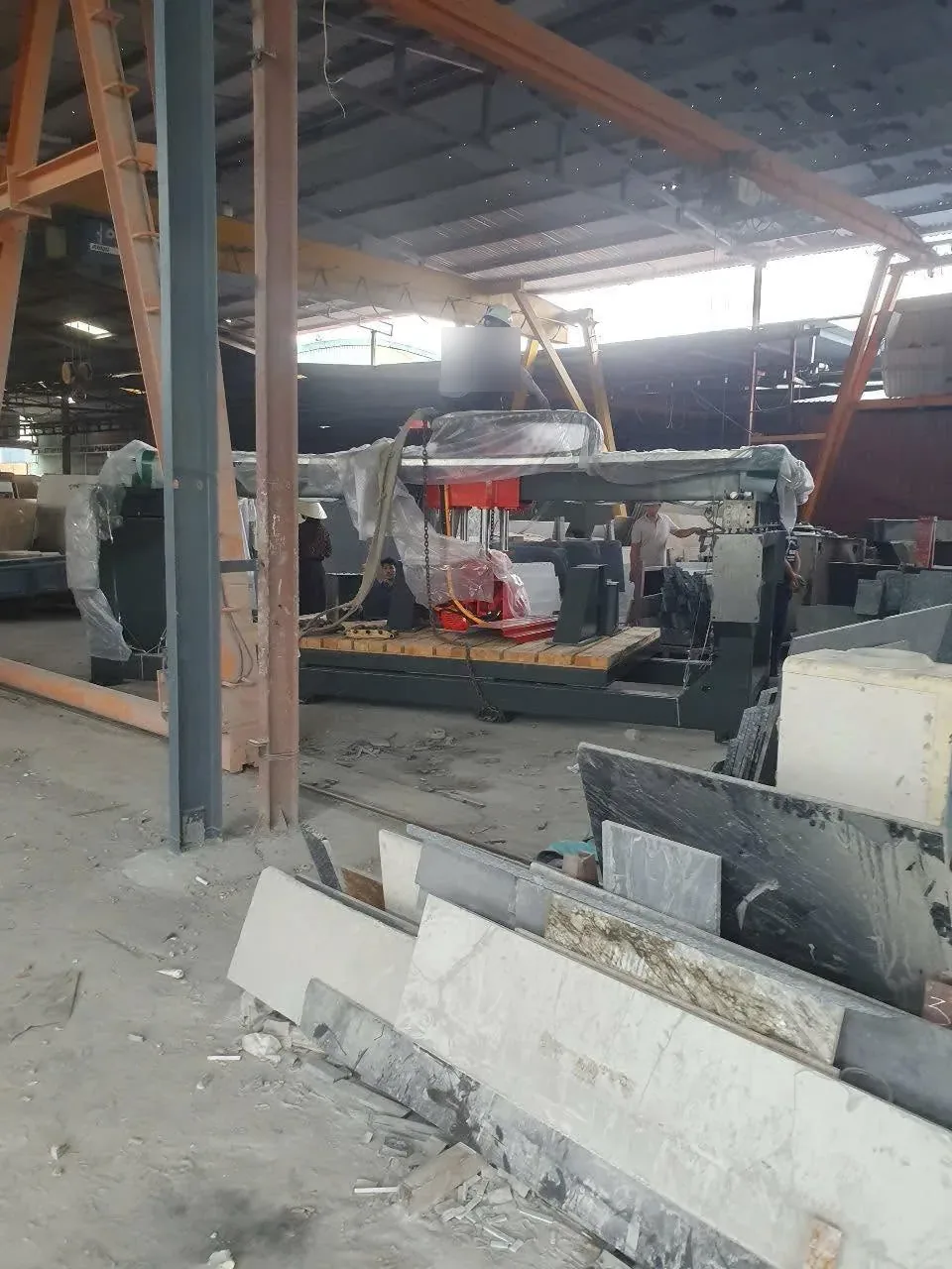 Thợ làm việc trên máy gia công đá trong xưởng có nhiều tấm đá xếp quanh tại Xe Nâng Đức Anh