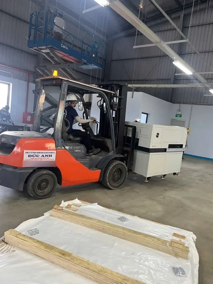 Xe nâng đưa máy sản xuất vào phòng xưởng, kiện gỗ kê trên pallet phủ bạt bên cạnh tại Hải Phòng