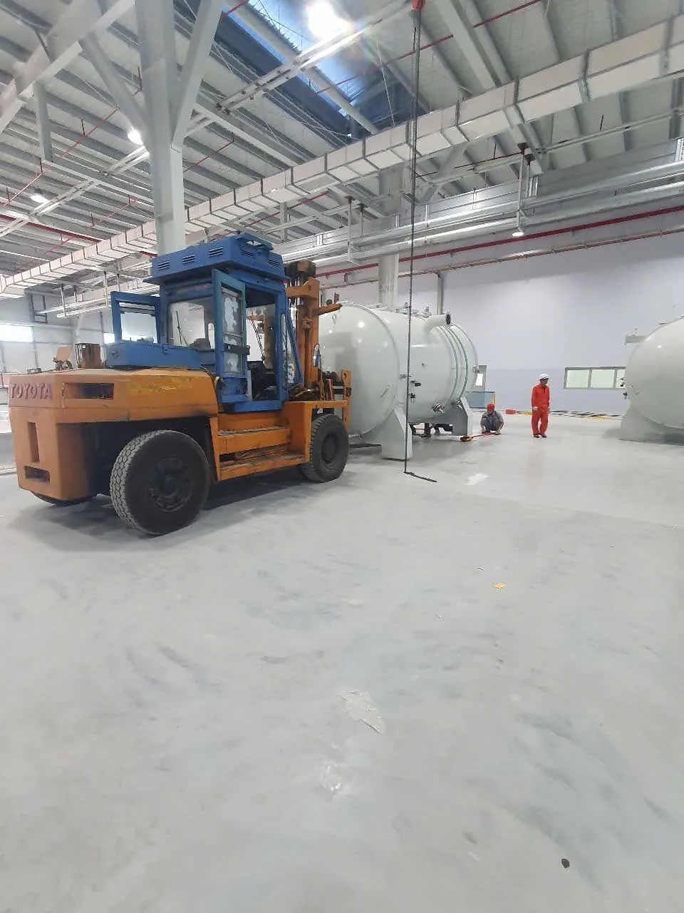 Xe nâng dầu cỡ lớn chạy giữa các bồn áp lực với công nhân quan sát phía xa tại Xe Nâng Đức Anh