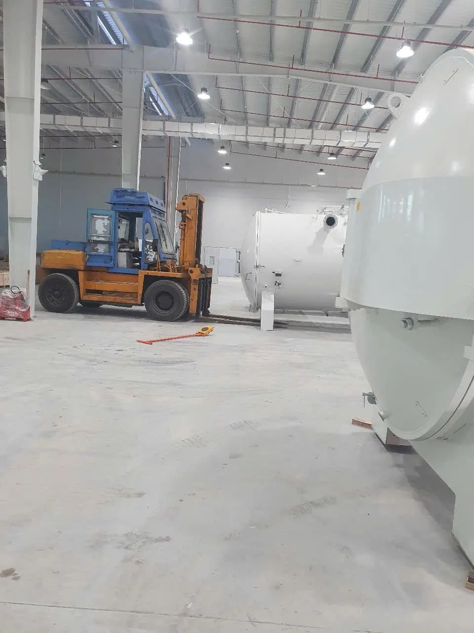 Xe nâng đứng cạnh thân bồn áp lực lớn khi căn vị trí trong xưởng tại Xe Nâng Đức Anh